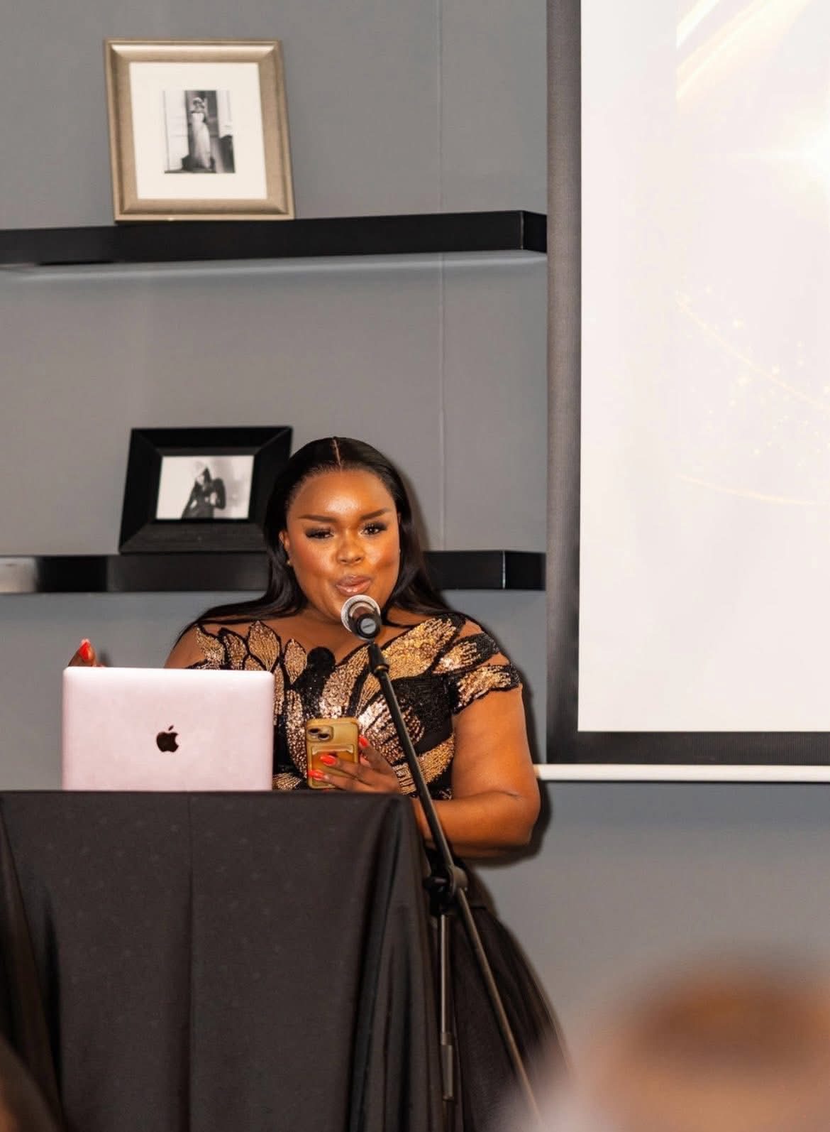 Segolame Thaga hosting from a lectern with a laptop and microphone