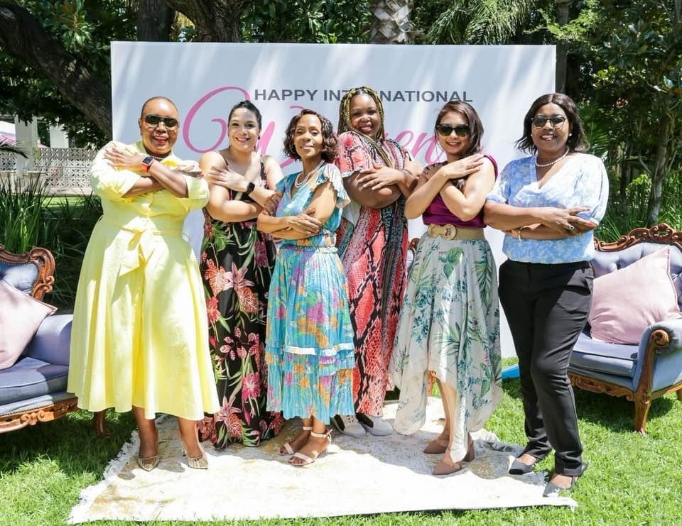 Guests at an outdoor International Women’s Day celebration, arms crossed in the Break the Bias pose in front of a Happy International Women’s Day backdrop