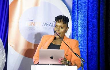 Segolame Thaga in an orange blazer at a lectern with a laptop